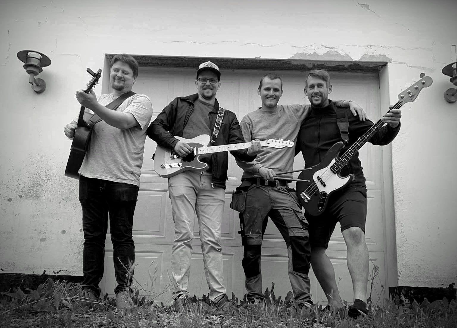 Reservatet. Fire musikere med guitar, trommer og bas foran garagen.